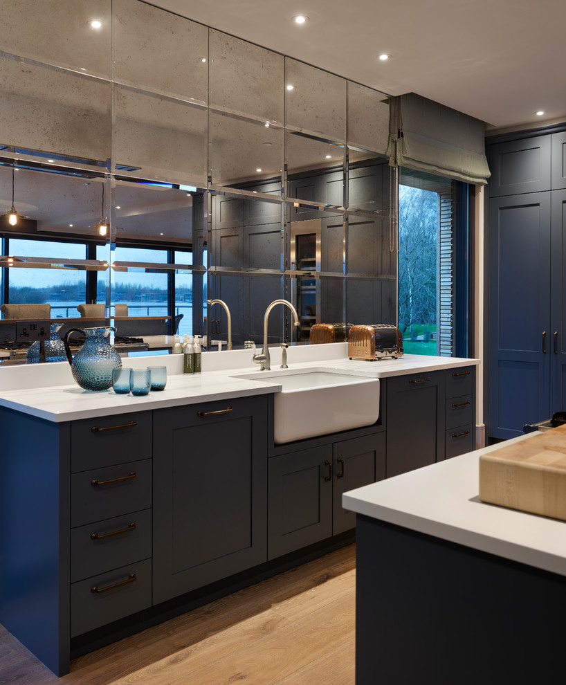 Idée de décoration pour une cuisine design avec un placard à porte shaker, des portes de placard bleues, une crédence métallisée, une crédence miroir, parquet clair, un sol beige et un plan de travail blanc.