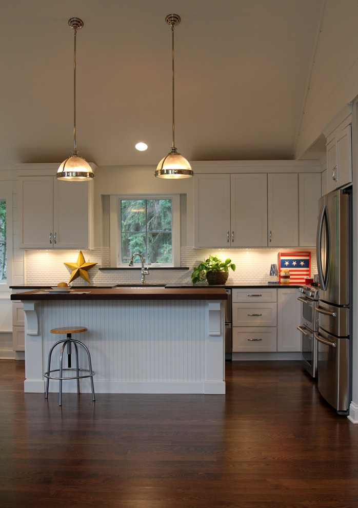 Eat-in kitchen - mid-sized transitional l-shaped medium tone wood floor eat-in kitchen idea in Milwaukee with a farmhouse sink, shaker cabinets, white cabinets, wood countertops, white backsplash, mosaic tile backsplash, stainless steel appliances and an island