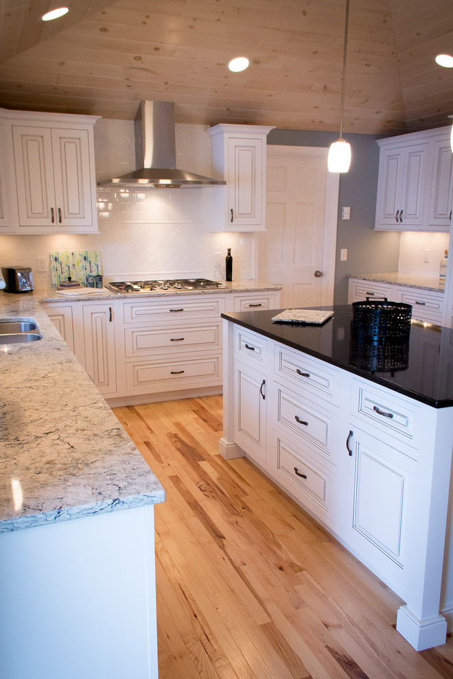 This is an example of a large coastal u-shaped kitchen/diner in Other with a submerged sink, raised-panel cabinets, white cabinets, engineered stone countertops, white splashback, metro tiled splashback, stainless steel appliances, light hardwood flooring and an island.