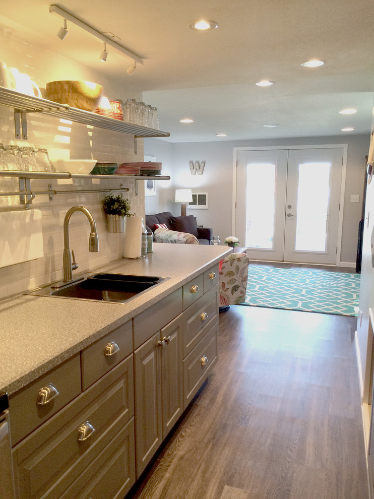 Modern inredning av ett litet kök, med en enkel diskho, luckor med infälld panel, grå skåp, laminatbänkskiva, vitt stänkskydd, stänkskydd i tunnelbanekakel, rostfria vitvaror och mellanmörkt trägolv