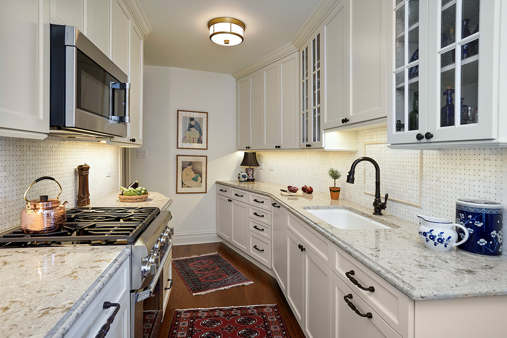 Klassisk inredning av ett litet grå grått kök, med en undermonterad diskho, luckor med glaspanel, beige skåp, bänkskiva i kvarts, beige stänkskydd, stänkskydd i marmor, integrerade vitvaror, ljust trägolv och brunt golv