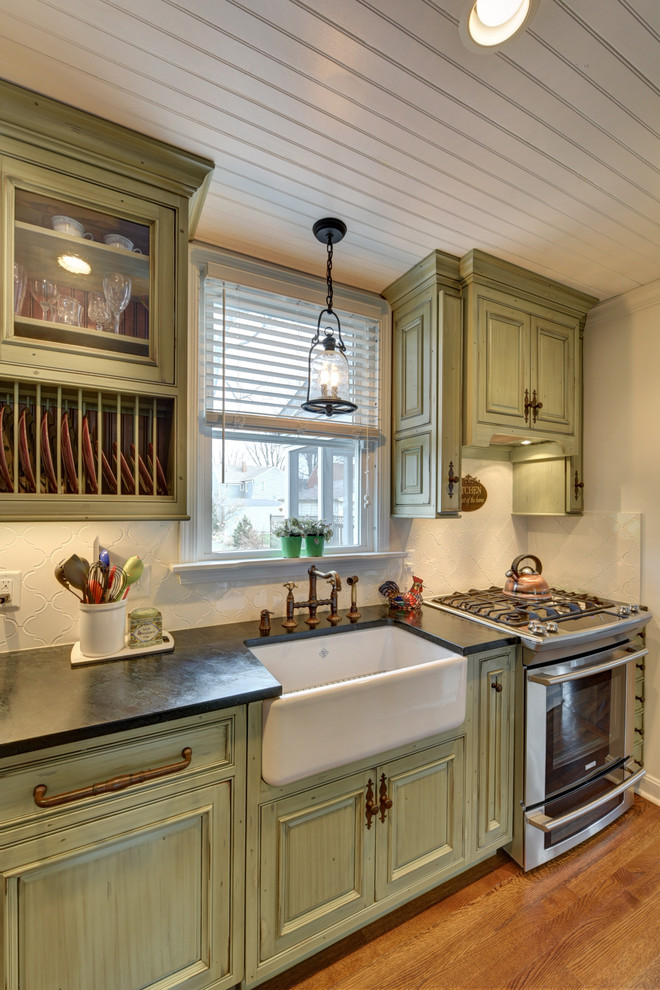 Inredning av ett lantligt kök, med en rustik diskho, luckor med upphöjd panel, skåp i slitet trä, vitt stänkskydd, rostfria vitvaror, mellanmörkt trägolv och brunt golv