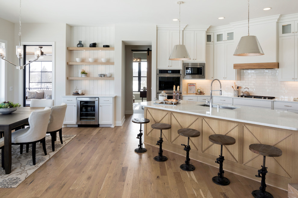 Inspiration for a farmhouse u-shaped kitchen/diner in Minneapolis with a submerged sink, shaker cabinets, white cabinets, white splashback, metro tiled splashback, stainless steel appliances, medium hardwood flooring, an island, brown floors and white worktops.