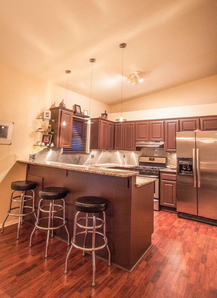 Example of a mid-sized trendy u-shaped laminate floor eat-in kitchen design in Oklahoma City with an undermount sink, raised-panel cabinets, brown cabinets, granite countertops, metallic backsplash, metal backsplash, stainless steel appliances and a peninsula