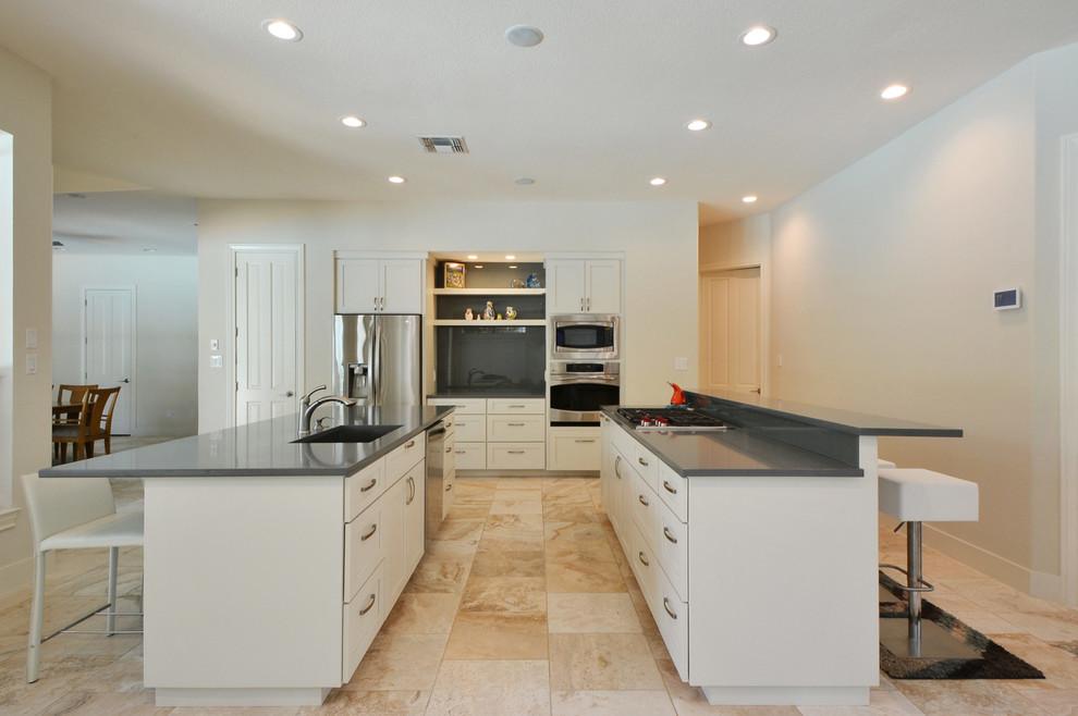 Example of a large trendy u-shaped travertine floor open concept kitchen design in Austin with an undermount sink, shaker cabinets, white cabinets, gray backsplash, glass sheet backsplash, stainless steel appliances, two islands and quartz countertops