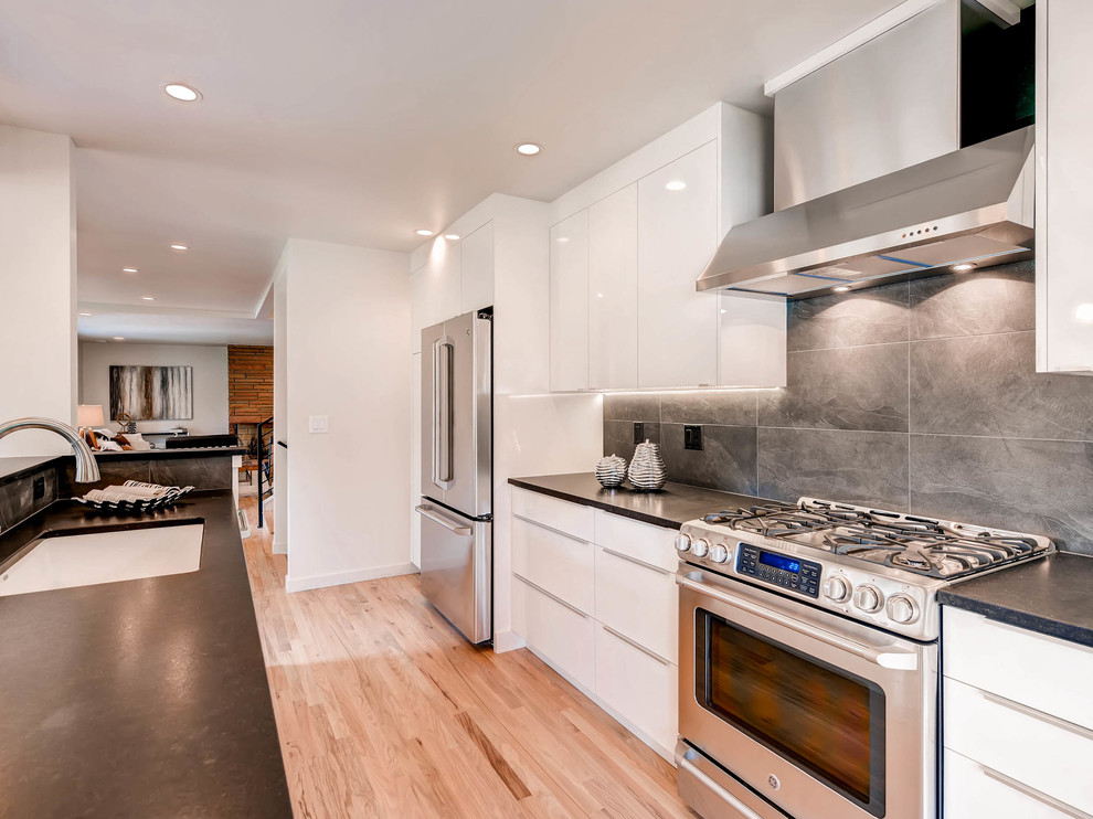 Zweizeilige Moderne Wohnküche mit Unterbauwaschbecken, flächenbündigen Schrankfronten, weißen Schränken, Küchenrückwand in Grau, Rückwand aus Stein, Küchengeräten aus Edelstahl, braunem Holzboden und Kücheninsel in Denver