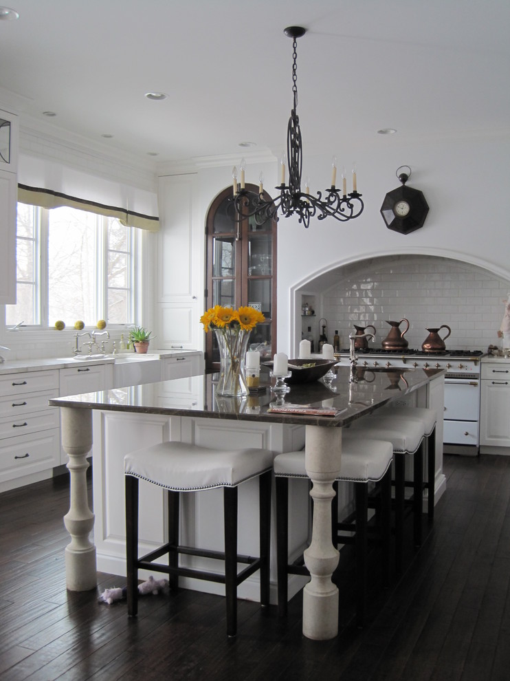 Mid-sized elegant u-shaped dark wood floor and brown floor eat-in kitchen photo in Detroit with a farmhouse sink, white backsplash, subway tile backsplash, white appliances, raised-panel cabinets, white cabinets, an island and white countertops