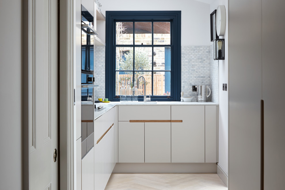Small contemporary l-shaped kitchen/diner in London with an integrated sink, flat-panel cabinets, white cabinets, granite worktops, beige splashback, ceramic splashback, stainless steel appliances, light hardwood flooring and no island.