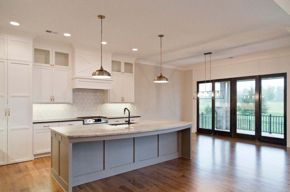 This is an example of a large traditional l-shaped open plan kitchen in Kansas City with a submerged sink, glass-front cabinets, white cabinets, granite worktops, white splashback, ceramic splashback, stainless steel appliances, medium hardwood flooring, an island, brown floors and grey worktops.