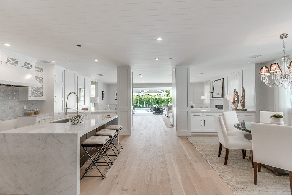 Example of a large trendy u-shaped light wood floor and brown floor eat-in kitchen design in Los Angeles with a drop-in sink, shaker cabinets, white cabinets, marble countertops, white backsplash, ceramic backsplash and an island