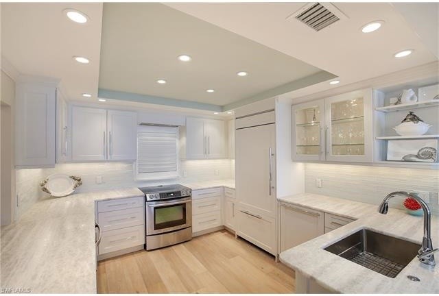 Example of a mid-sized beach style u-shaped light wood floor enclosed kitchen design in Miami with an undermount sink, shaker cabinets, white cabinets, onyx countertops, white backsplash, glass tile backsplash, paneled appliances and no island