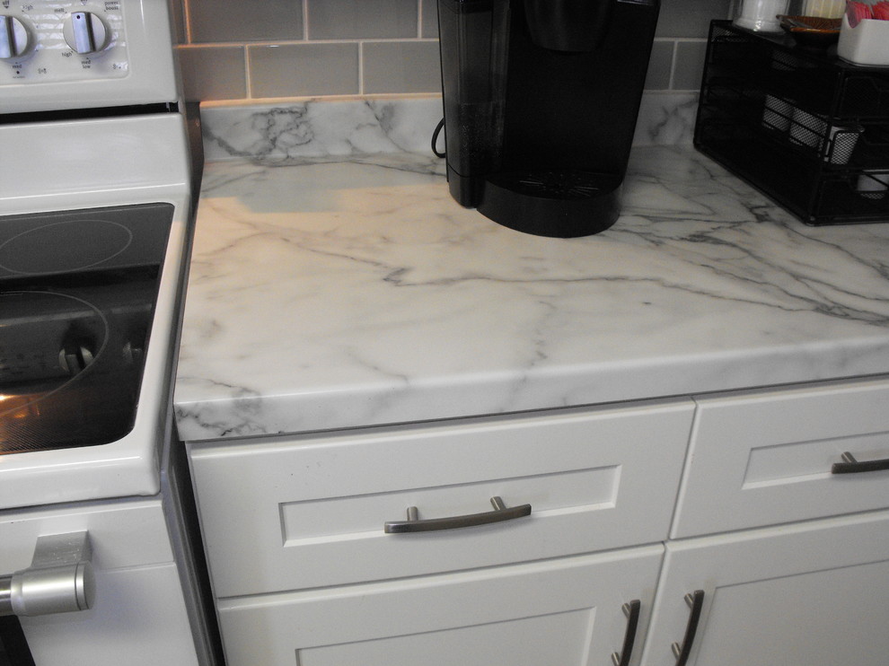 Bild på ett mellanstort l-kök, med en nedsänkt diskho, skåp i shakerstil, vita skåp, laminatbänkskiva, grått stänkskydd, stänkskydd i keramik och vita vitvaror