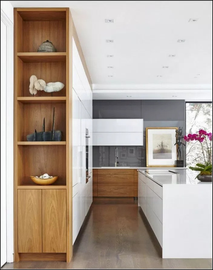 Inredning av ett modernt stort vit vitt kök, med en undermonterad diskho, släta luckor, vita skåp, bänkskiva i kvarts, grått stänkskydd, glaspanel som stänkskydd, svarta vitvaror, ljust trägolv, en köksö och brunt golv
