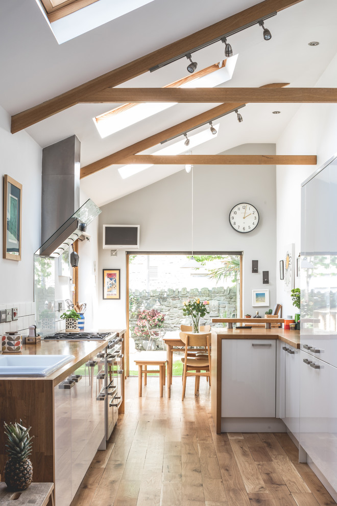 Mid-sized farmhouse u-shaped medium tone wood floor and brown floor open concept kitchen photo in Other with flat-panel cabinets, white cabinets, wood countertops, white backsplash, paneled appliances, a peninsula, brown countertops and a drop-in sink