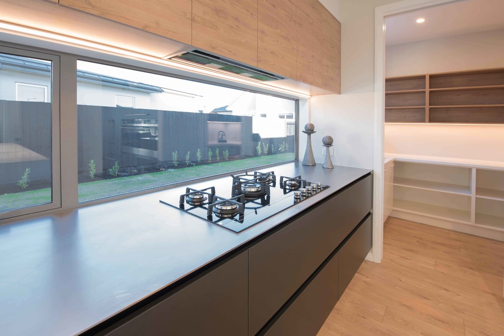 Medium sized contemporary galley kitchen/diner in Christchurch with a submerged sink, flat-panel cabinets, grey cabinets, engineered stone countertops, window splashback, stainless steel appliances, light hardwood flooring, an island, brown floors and white worktops.