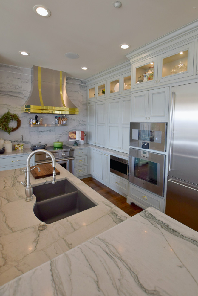 Klassisk inredning av ett stort kök, med en undermonterad diskho, luckor med profilerade fronter, grå skåp, vitt stänkskydd, stänkskydd i marmor, rostfria vitvaror, mellanmörkt trägolv och en köksö