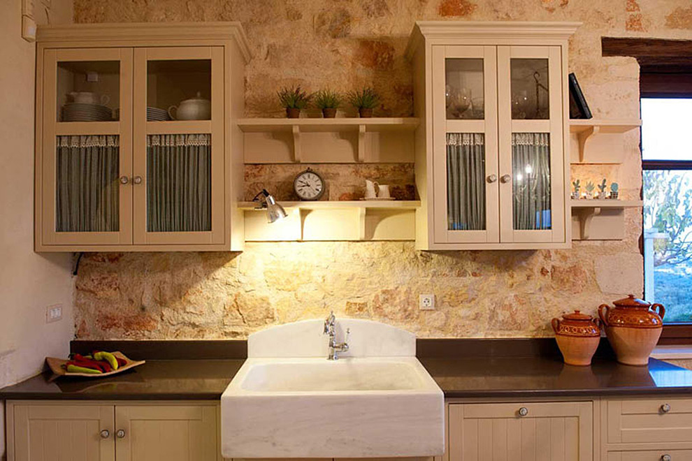 Esempio di una cucina mediterranea di medie dimensioni con lavello stile country, ante di vetro, ante con finitura invecchiata, top in granito, paraspruzzi beige, paraspruzzi con piastrelle in pietra, elettrodomestici in acciaio inossidabile e pavimento in pietra calcarea