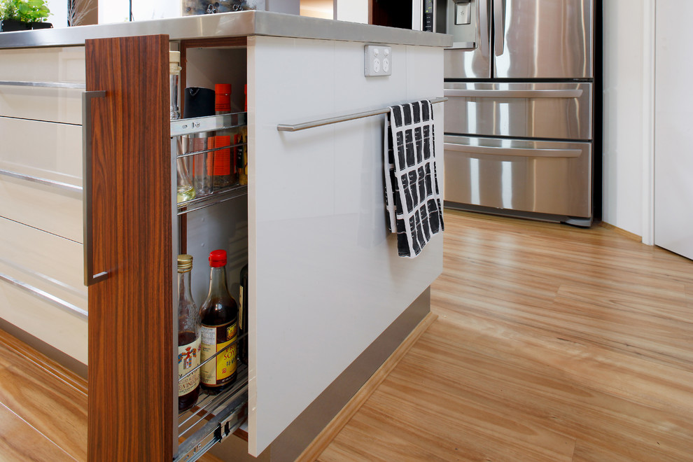 Modern inredning av ett mellanstort kök, med en undermonterad diskho, släta luckor, vita skåp, granitbänkskiva, stänkskydd med metallisk yta, stänkskydd i glaskakel, svarta vitvaror, mellanmörkt trägolv och en köksö