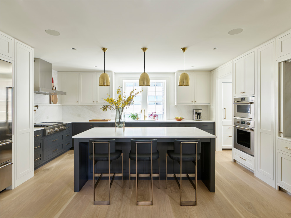 Traditional u-shaped kitchen in Philadelphia with a submerged sink, shaker cabinets, white cabinets, white splashback, stone slab splashback, stainless steel appliances, light hardwood flooring, an island, beige floors and white worktops.