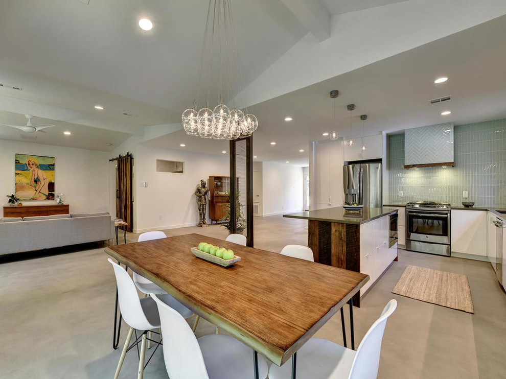 Example of a mid-sized minimalist galley concrete floor open concept kitchen design in Austin with an undermount sink, flat-panel cabinets, white cabinets, quartz countertops, green backsplash, glass tile backsplash, stainless steel appliances and an island