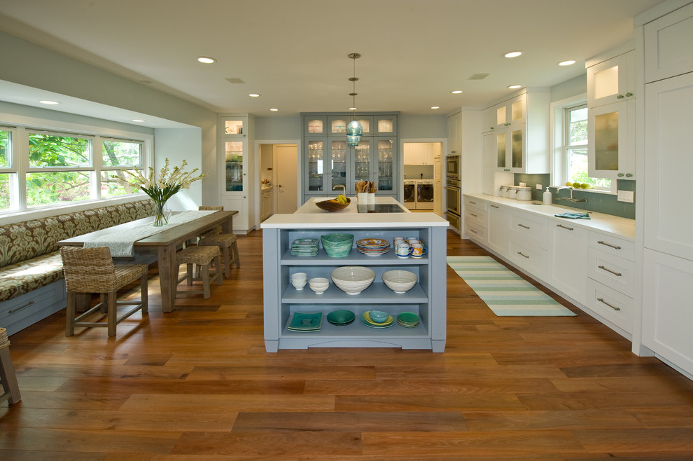 Example of an island style kitchen pantry design in Hawaii with an integrated sink, shaker cabinets, white cabinets, solid surface countertops, blue backsplash, glass tile backsplash, paneled appliances and an island
