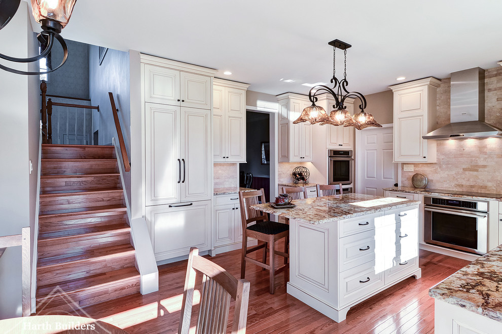 Example of a mid-sized classic l-shaped medium tone wood floor eat-in kitchen design in Philadelphia with an undermount sink, raised-panel cabinets, white cabinets, granite countertops, beige backsplash, stone tile backsplash, stainless steel appliances and an island