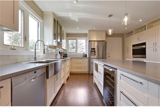 Foto på ett mellanstort funkis kök, med en rustik diskho, luckor med upphöjd panel, vita skåp, bänkskiva i kvartsit, vitt stänkskydd, stänkskydd i glaskakel, rostfria vitvaror, mörkt trägolv och en köksö