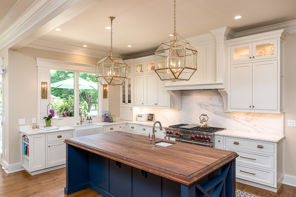 Example of a classic l-shaped medium tone wood floor kitchen design in Other with a farmhouse sink, shaker cabinets, white cabinets, white backsplash, stainless steel appliances and an island