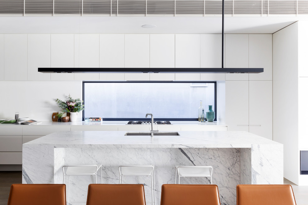 Immagine di una cucina minimal con lavello sottopiano, ante lisce, ante bianche, paraspruzzi a finestra, elettrodomestici da incasso, pavimento marrone e top grigio