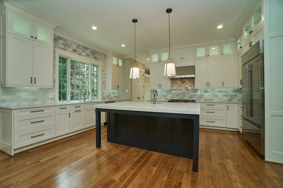 Large traditional u-shaped open plan kitchen in DC Metro with a submerged sink, shaker cabinets, white cabinets, engineered stone countertops, grey splashback, marble splashback, stainless steel appliances, medium hardwood flooring, an island, brown floors and white worktops.
