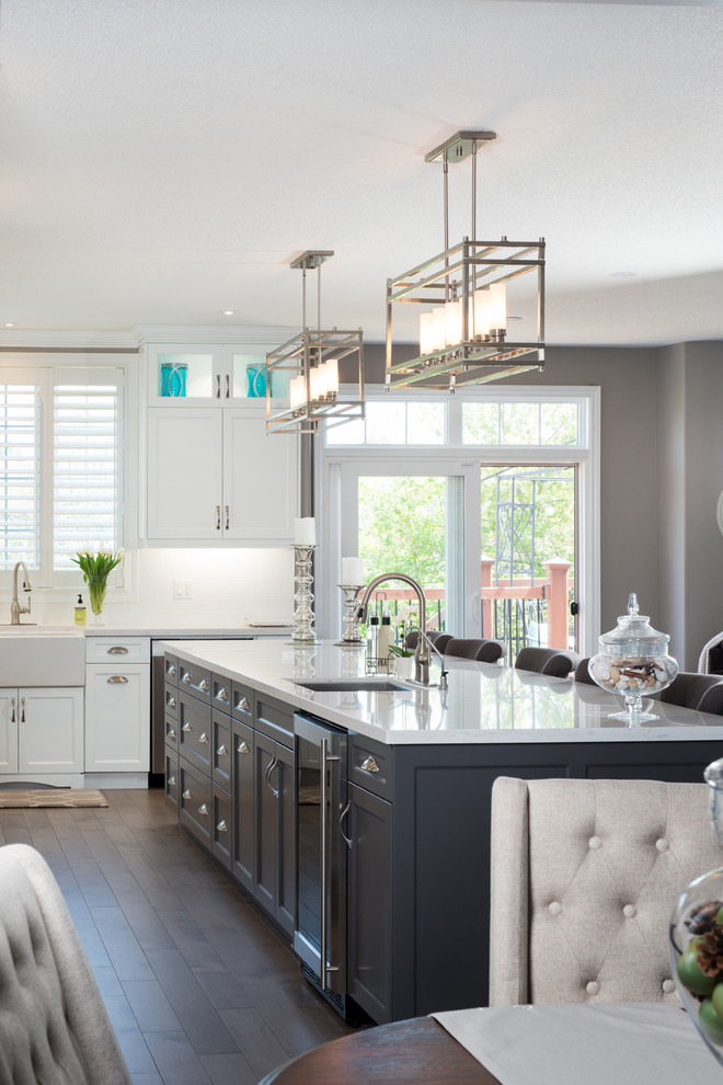 Large traditional l-shaped kitchen/diner in Toronto with a belfast sink, recessed-panel cabinets, white cabinets, engineered stone countertops, white splashback, ceramic splashback, stainless steel appliances, medium hardwood flooring and an island.