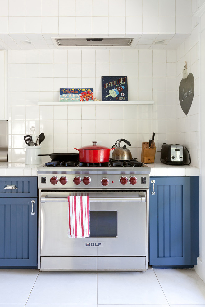 Inspiration pour une grande cuisine traditionnelle avec un placard avec porte à panneau encastré, des portes de placard bleues, plan de travail carrelé, une crédence blanche, un électroménager en acier inoxydable et un sol blanc.