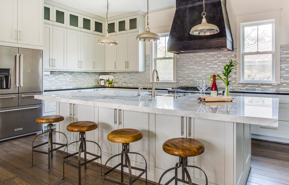 Inspiration for a farmhouse l-shaped kitchen in Houston with a double-bowl sink, shaker cabinets, white cabinets, grey splashback, stainless steel appliances, dark hardwood flooring, an island and brown floors.