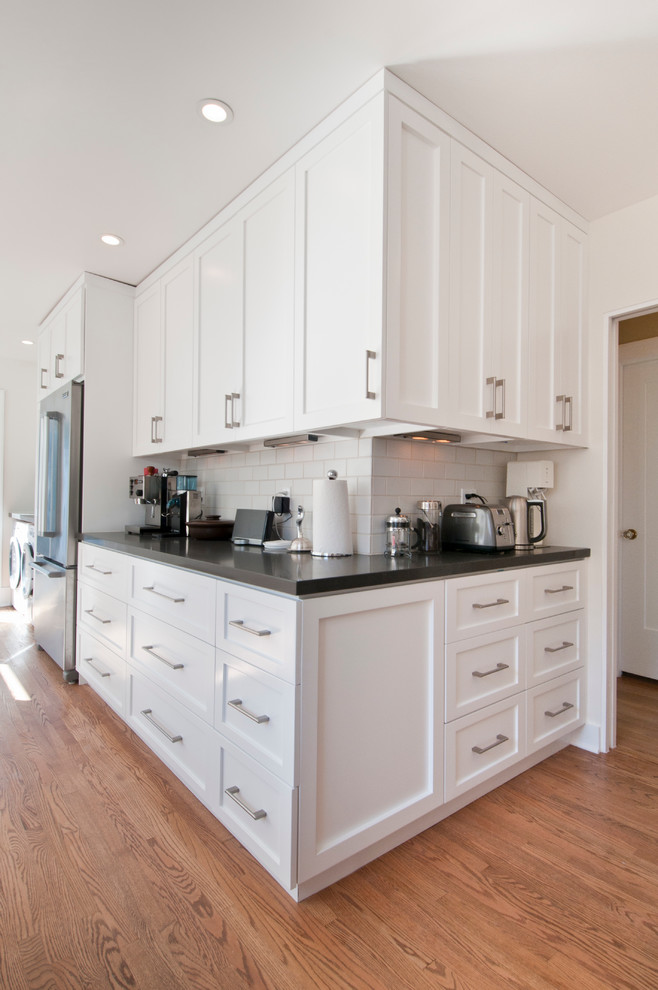 This is an example of a medium sized classic l-shaped kitchen pantry in Los Angeles with a submerged sink, shaker cabinets, white cabinets, engineered stone countertops, grey splashback, metro tiled splashback, stainless steel appliances, medium hardwood flooring and no island.