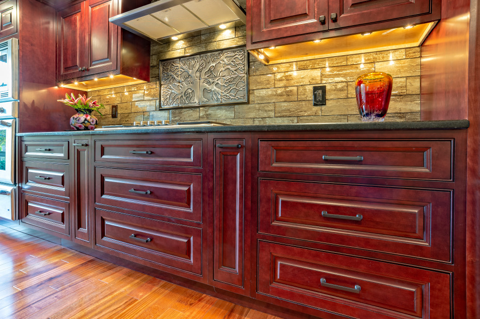 Idéer för ett stort klassiskt brun linjärt kök och matrum, med en undermonterad diskho, luckor med upphöjd panel, röda skåp, granitbänkskiva, brunt stänkskydd, stänkskydd i porslinskakel, rostfria vitvaror, ljust trägolv, en köksö och brunt golv