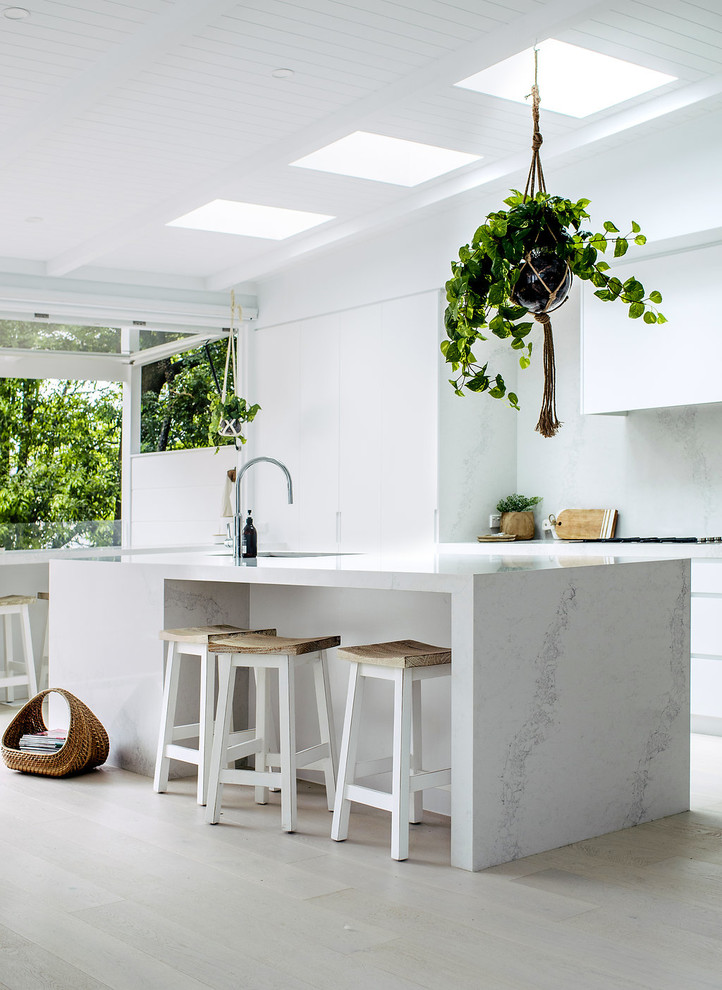 Coastal kitchen in Sydney with a submerged sink, flat-panel cabinets, white cabinets, grey splashback, light hardwood flooring, an island and beige floors.
