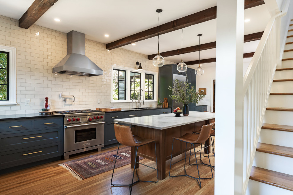 Large country l-shaped light wood floor eat-in kitchen photo in Portland with an undermount sink, shaker cabinets, blue cabinets, soapstone countertops, white backsplash, subway tile backsplash, stainless steel appliances, an island and black countertops