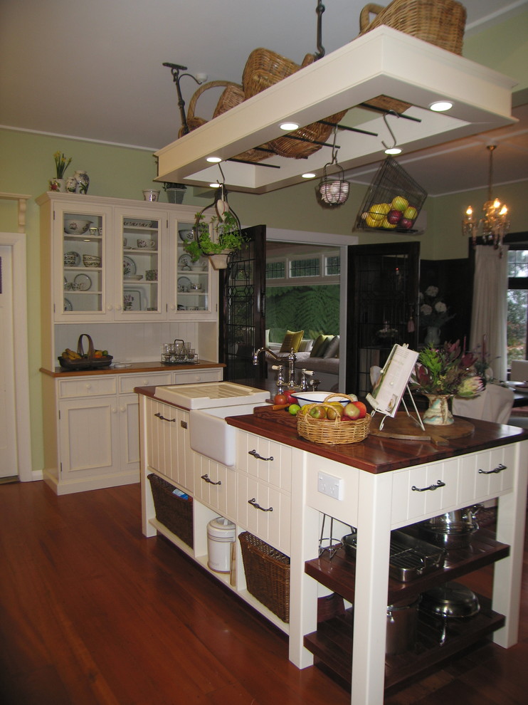 Inspiration for a mid-sized country u-shaped medium tone wood floor and brown floor eat-in kitchen remodel in Wellington with a drop-in sink, raised-panel cabinets, white cabinets, wood countertops, white backsplash, subway tile backsplash, stainless steel appliances, an island and brown countertops
