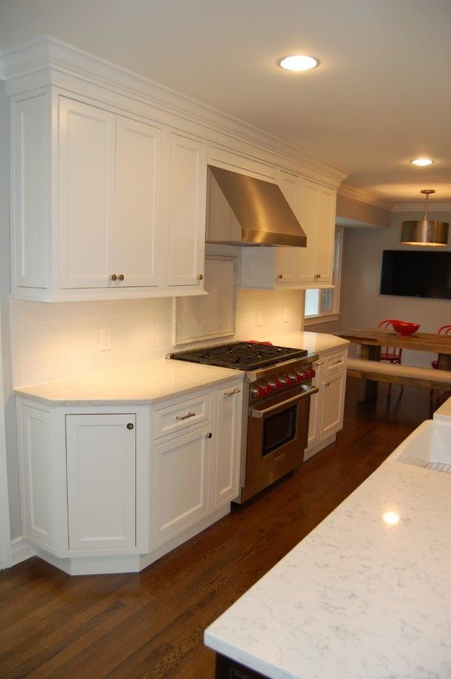 Example of a mid-sized eclectic l-shaped dark wood floor eat-in kitchen design in New York with a farmhouse sink, shaker cabinets, white cabinets, quartz countertops, white backsplash, stainless steel appliances and an island