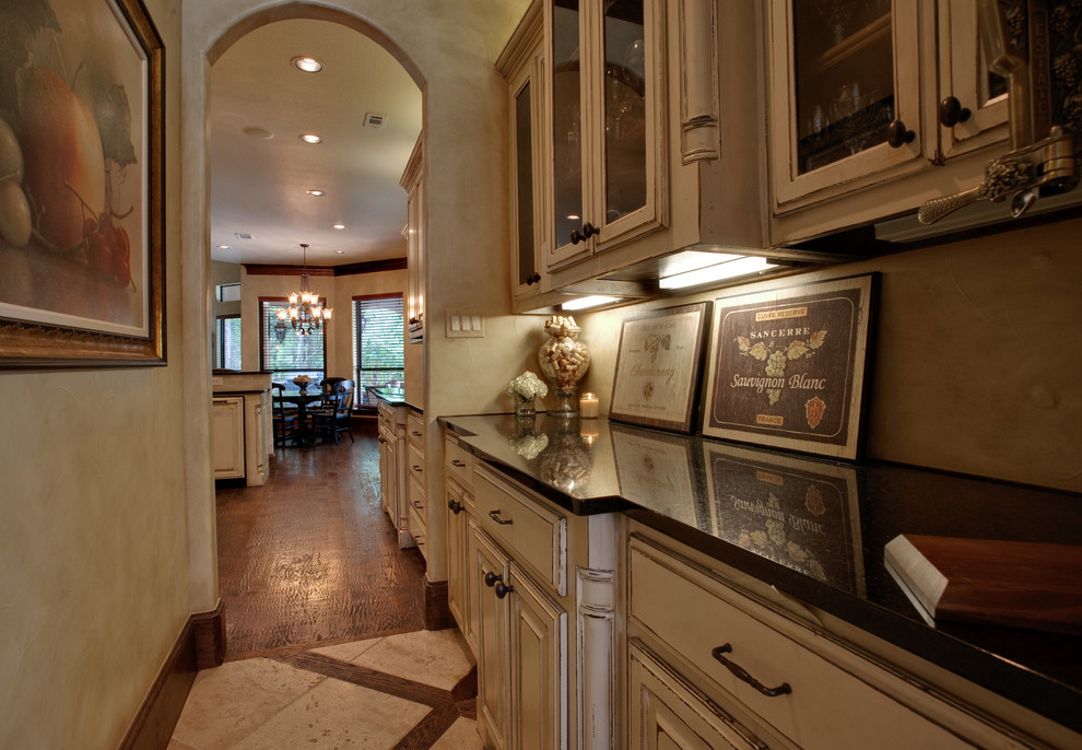 Aménagement d'une cuisine américaine parallèle classique de taille moyenne avec un plan de travail en granite, une crédence beige, des portes de placard beiges, une crédence en carrelage de pierre et un sol en travertin.