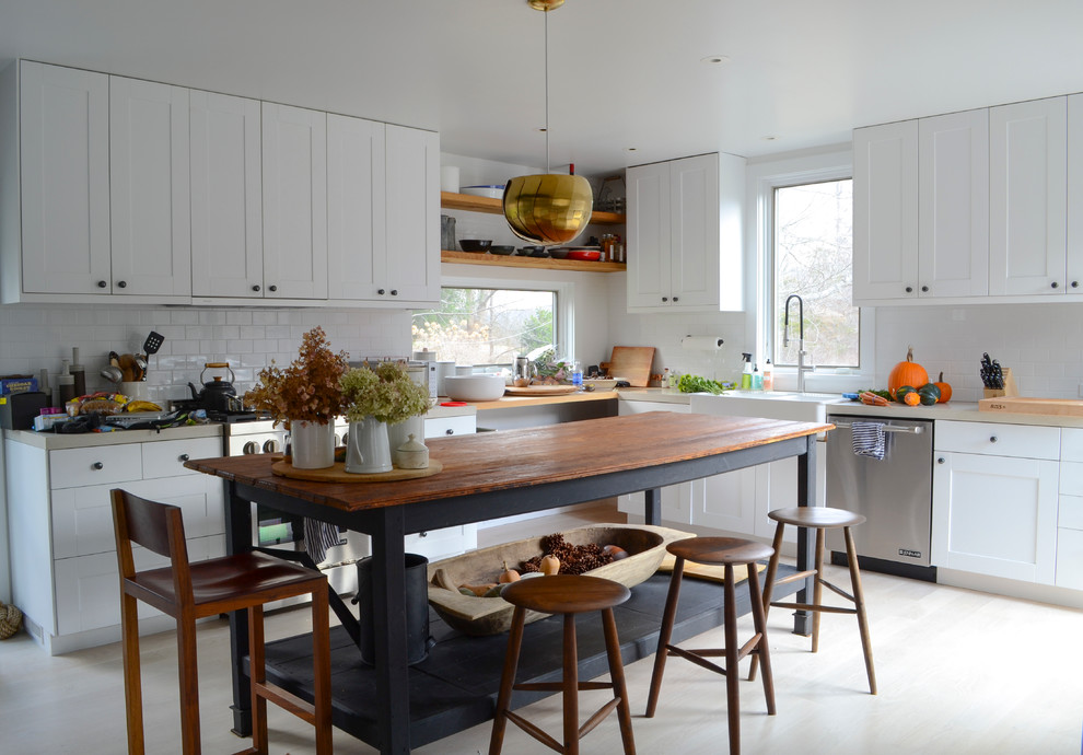 Bild på ett stort lantligt kök, med en dubbel diskho, släta luckor, vita skåp, granitbänkskiva, vitt stänkskydd, stänkskydd i keramik, rostfria vitvaror och laminatgolv