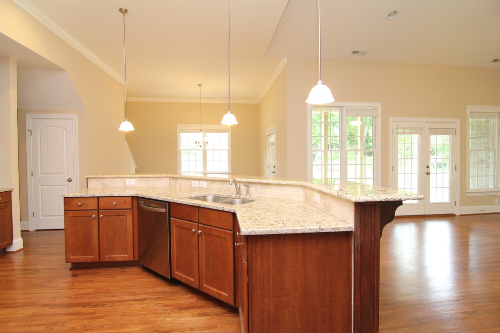 Photo of a large traditional u-shaped open plan kitchen in Raleigh with a double-bowl sink, recessed-panel cabinets, medium wood cabinets, granite worktops, beige splashback, ceramic splashback, stainless steel appliances, medium hardwood flooring and an island.