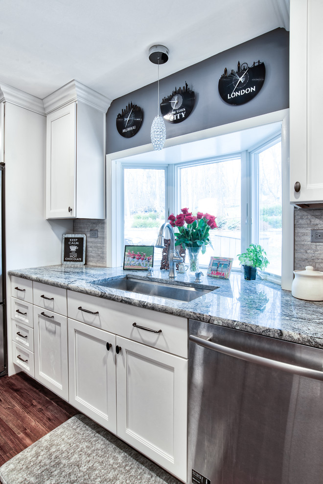 Inspiration for a mid-sized timeless l-shaped dark wood floor eat-in kitchen remodel in New York with an undermount sink, shaker cabinets, white cabinets, gray backsplash, stone tile backsplash, stainless steel appliances, an island and multicolored countertops