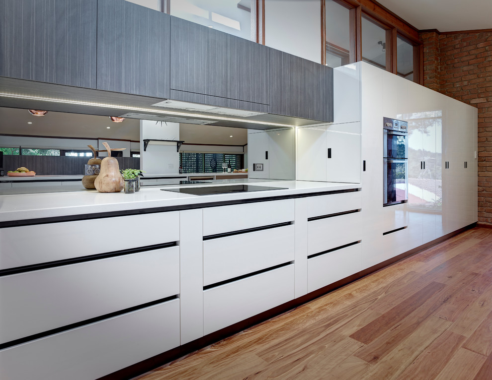 Inredning av ett modernt stort kök, med en dubbel diskho, vita skåp, laminatbänkskiva, glaspanel som stänkskydd, rostfria vitvaror och mellanmörkt trägolv
