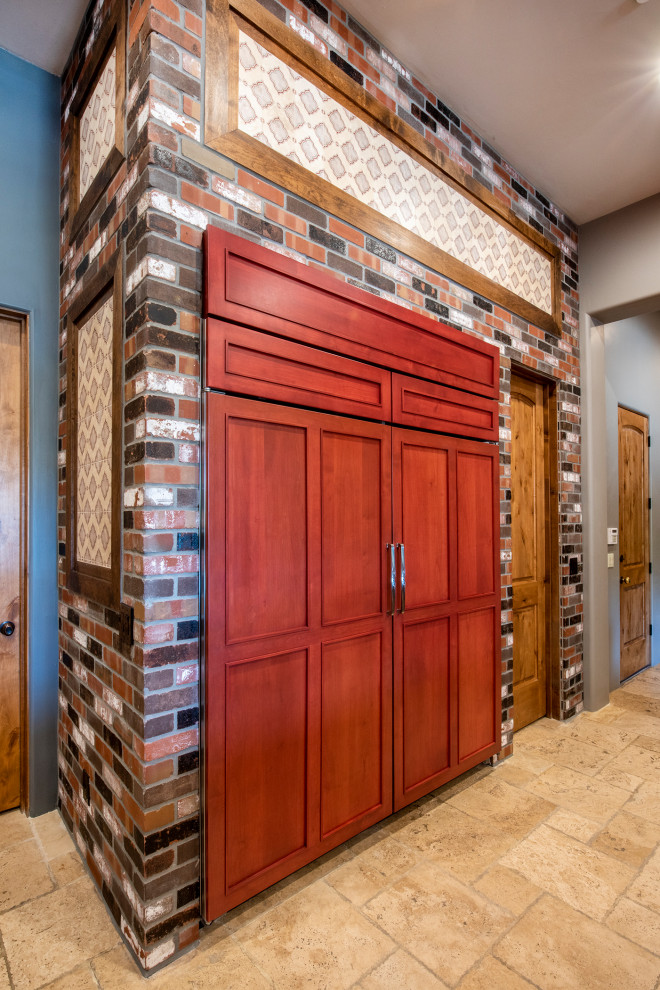 Huge arts and crafts l-shaped travertine floor and beige floor open concept kitchen photo in Phoenix with a farmhouse sink, shaker cabinets, brown cabinets, granite countertops, metallic backsplash, metal backsplash, stainless steel appliances, two islands and red countertops