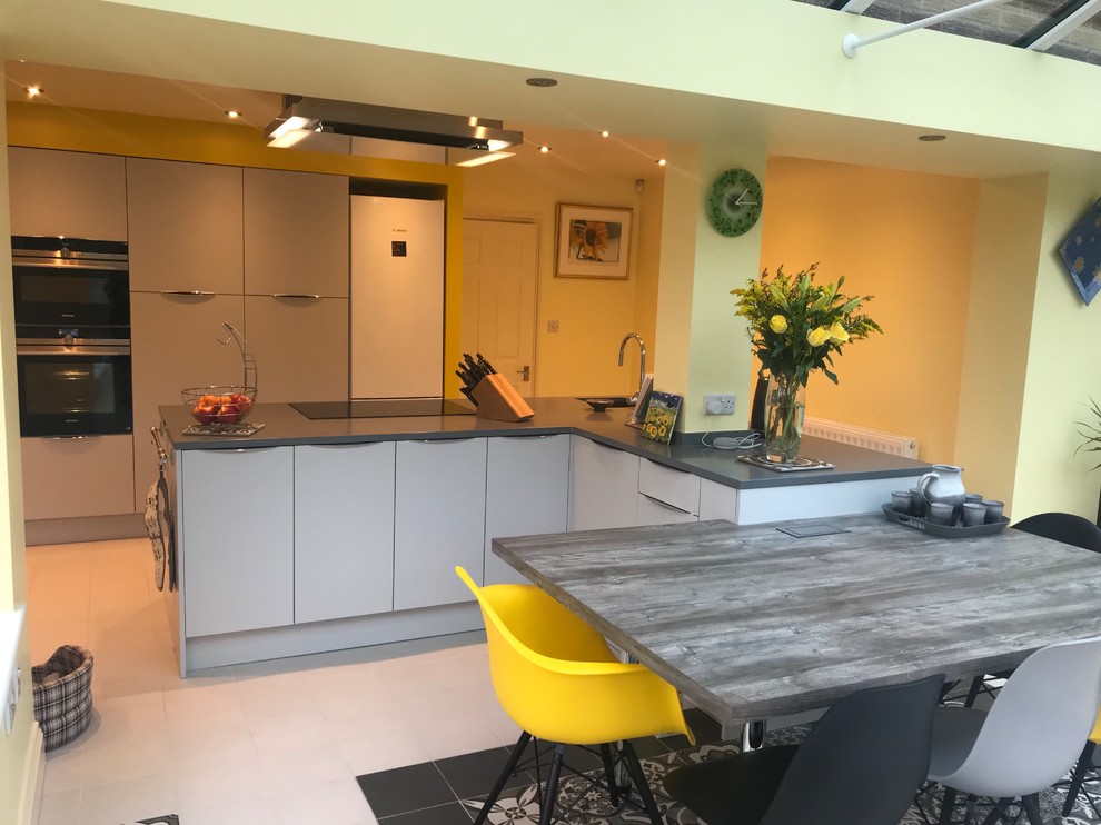 This is an example of a large contemporary l-shaped open plan kitchen in Buckinghamshire with a submerged sink, flat-panel cabinets, grey cabinets, quartz worktops, multi-coloured splashback, glass sheet splashback, integrated appliances, ceramic flooring, an island, grey floors and grey worktops.