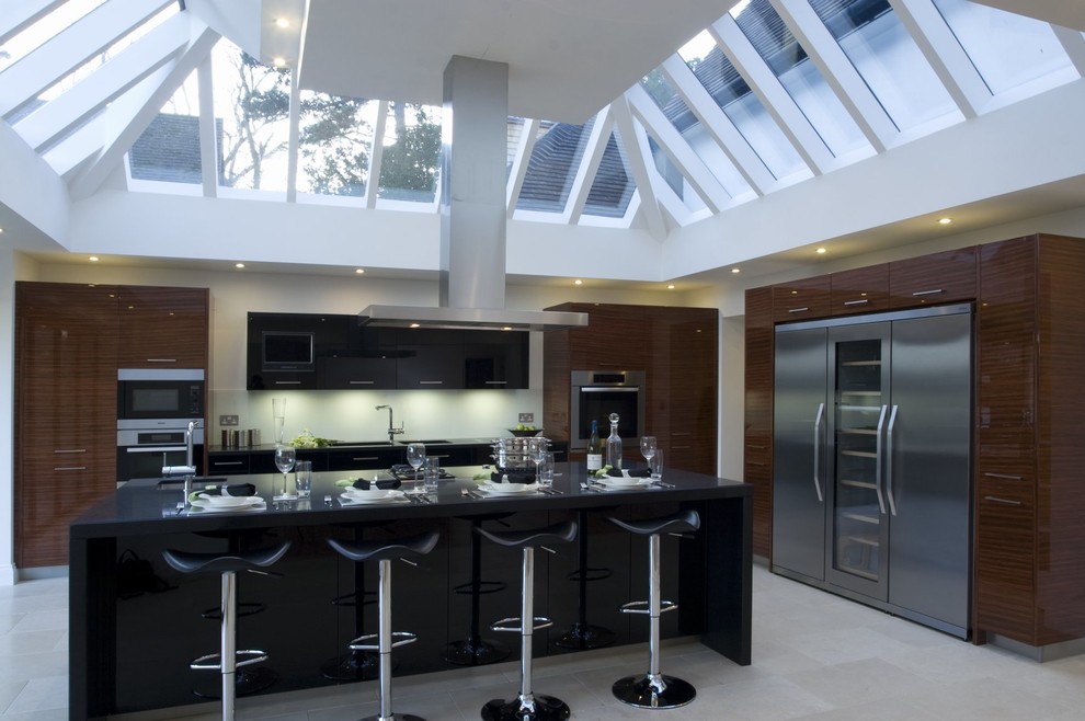 This is an example of a medium sized contemporary l-shaped open plan kitchen in Buckinghamshire with a built-in sink, flat-panel cabinets, medium wood cabinets, granite worktops, yellow splashback, glass sheet splashback, stainless steel appliances, limestone flooring and an island.