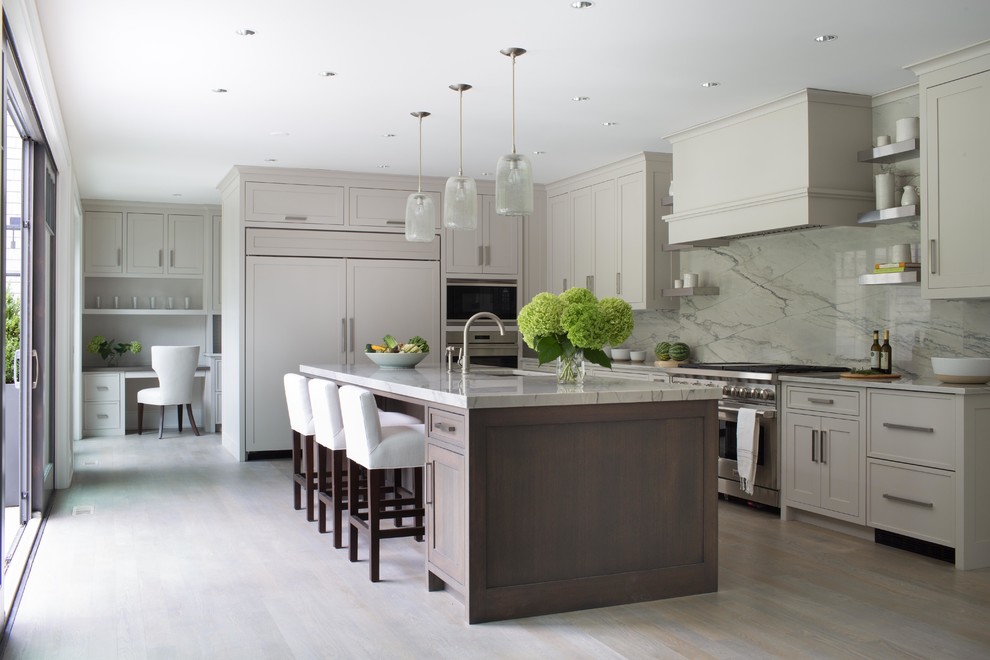 Example of a transitional light wood floor kitchen design in New York with an undermount sink, shaker cabinets, beige cabinets, white backsplash, stone slab backsplash, paneled appliances and an island