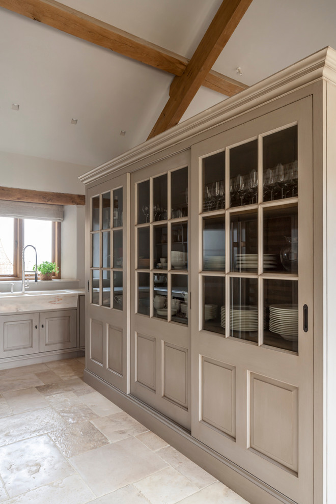 Large rustic galley open plan kitchen in Gloucestershire with a single-bowl sink, raised-panel cabinets, marble worktops, stone slab splashback, stainless steel appliances, limestone flooring, an island and beige cabinets.