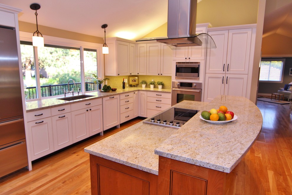 Inspiration for a large timeless l-shaped medium tone wood floor open concept kitchen remodel in Portland with an undermount sink, recessed-panel cabinets, white cabinets, granite countertops, glass tile backsplash, stainless steel appliances, an island and multicolored countertops